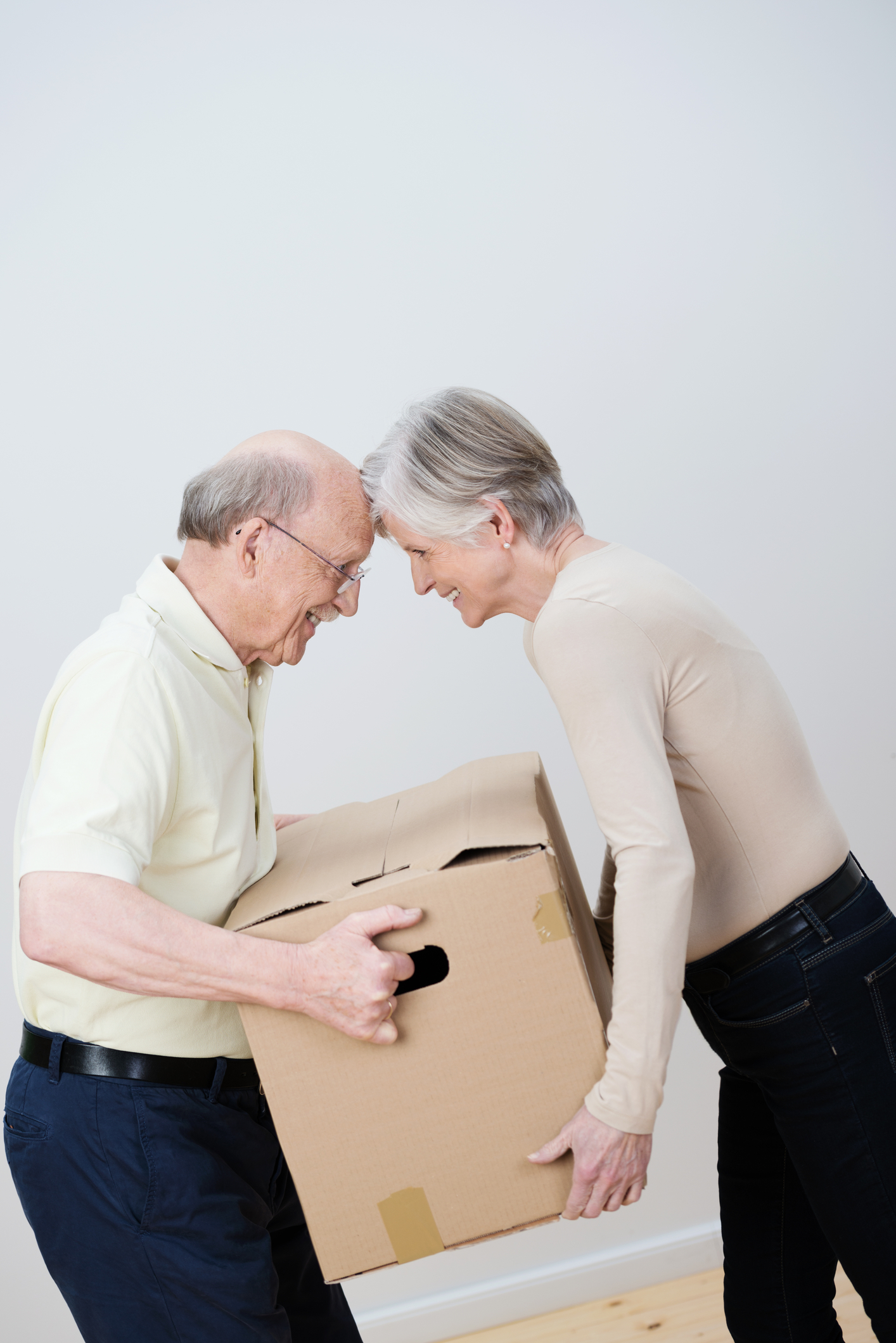 two senior citizens carry a moving box together